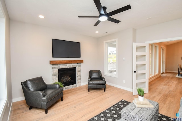 sitting room featuring hardwood / wood-style flooring, ceiling fan, and a stone fireplace