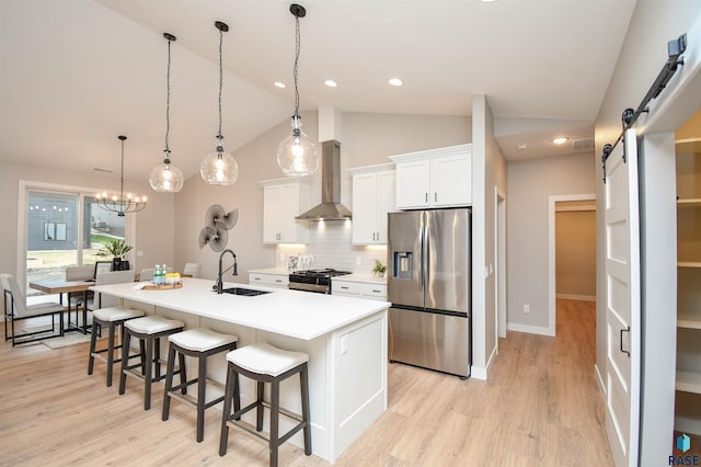 kitchen featuring appliances with stainless steel finishes, wall chimney exhaust hood, sink, a barn door, and white cabinetry