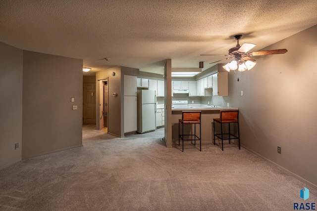 kitchen with white cabinetry, a kitchen breakfast bar, a textured ceiling, white appliances, and light carpet