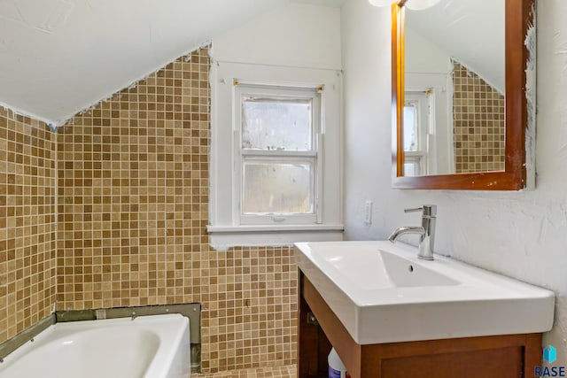 bathroom featuring a bathing tub, vanity, tile walls, and vaulted ceiling