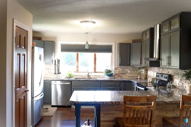 kitchen with sink, wall chimney exhaust hood, dark stone countertops, decorative light fixtures, and appliances with stainless steel finishes