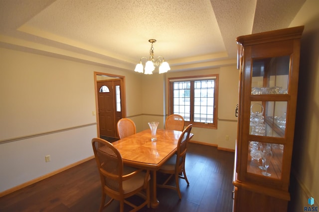 dining space with a raised ceiling, a chandelier, dark wood-type flooring, and a textured ceiling