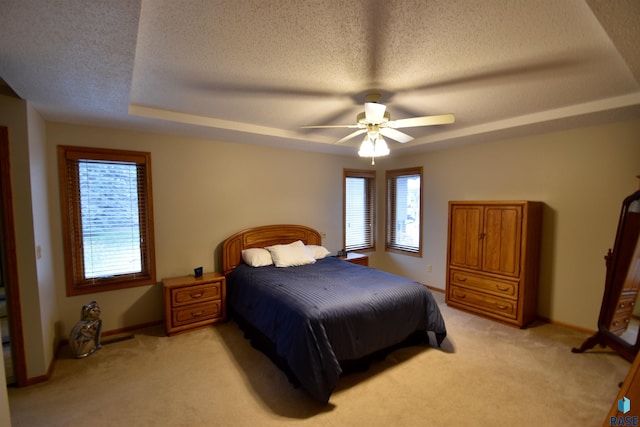 carpeted bedroom featuring a tray ceiling, ceiling fan, and a textured ceiling