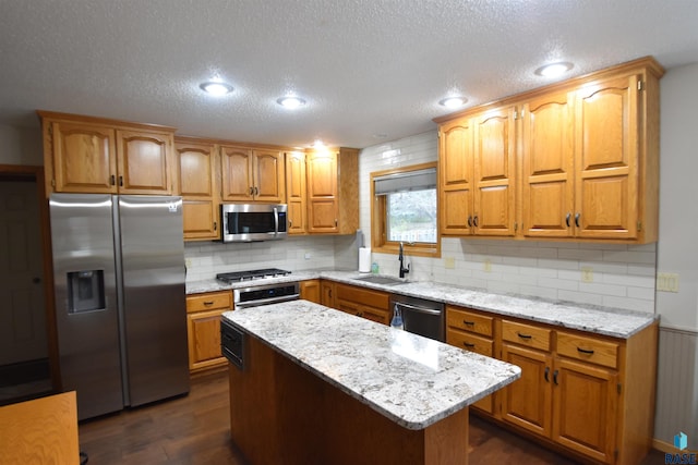 kitchen featuring appliances with stainless steel finishes, dark hardwood / wood-style flooring, light stone counters, sink, and a kitchen island