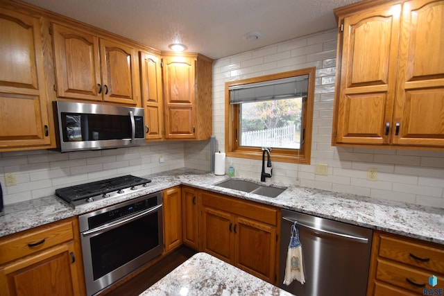 kitchen featuring stainless steel appliances, light stone counters, tasteful backsplash, and sink