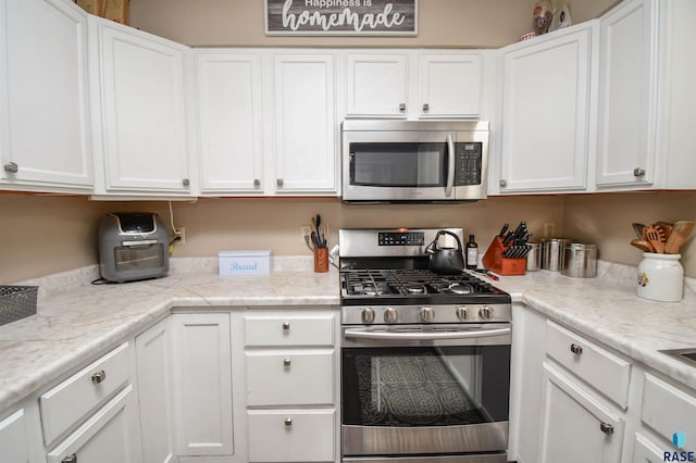 kitchen with light stone counters, white cabinets, and appliances with stainless steel finishes