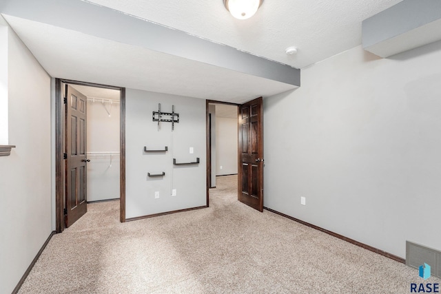 unfurnished bedroom featuring light colored carpet, a walk in closet, a textured ceiling, and a closet