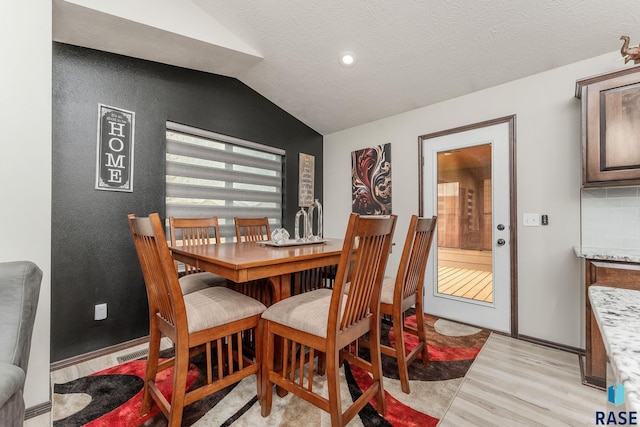 dining area featuring light hardwood / wood-style floors, a textured ceiling, and vaulted ceiling