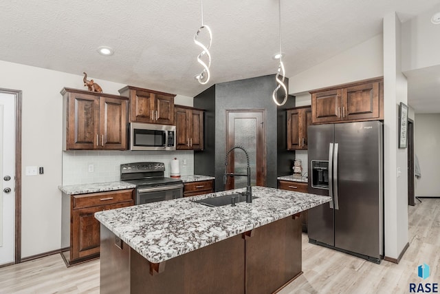 kitchen featuring sink, a kitchen island with sink, vaulted ceiling, decorative backsplash, and appliances with stainless steel finishes