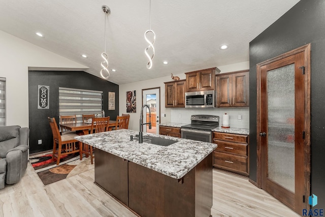 kitchen with light stone countertops, appliances with stainless steel finishes, tasteful backsplash, light hardwood / wood-style flooring, and an island with sink