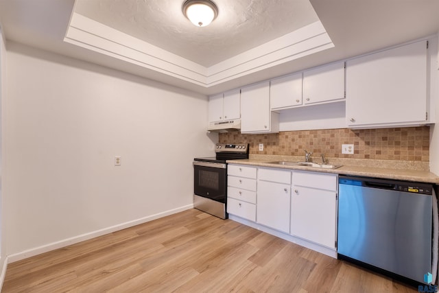 kitchen with sink, appliances with stainless steel finishes, a tray ceiling, light hardwood / wood-style floors, and white cabinetry