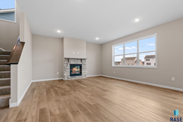 unfurnished living room featuring a stone fireplace and light hardwood / wood-style flooring