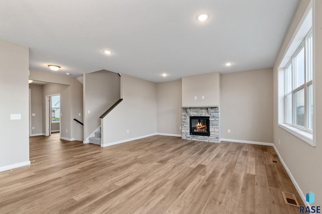 unfurnished living room with light hardwood / wood-style floors and a stone fireplace