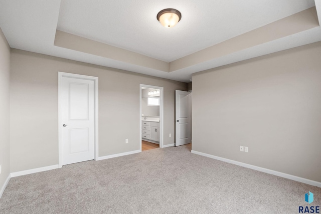 unfurnished bedroom featuring light carpet, connected bathroom, a tray ceiling, and a closet