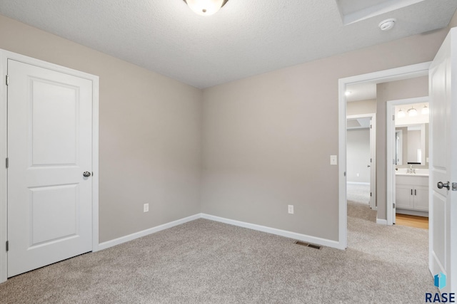 unfurnished bedroom featuring light carpet, a textured ceiling, sink, and connected bathroom