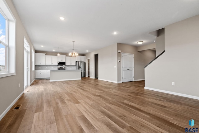 unfurnished living room featuring sink, light hardwood / wood-style floors, and a notable chandelier