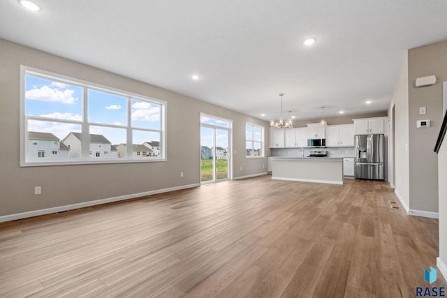 unfurnished living room with sink, light hardwood / wood-style floors, and a notable chandelier