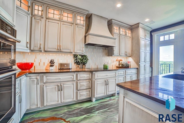 kitchen featuring sink, premium range hood, cream cabinetry, decorative backsplash, and black appliances