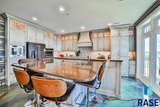 kitchen with a large island, stainless steel appliances, premium range hood, backsplash, and a breakfast bar