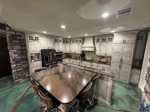 kitchen featuring black appliances, tasteful backsplash, a large island, custom range hood, and a breakfast bar area