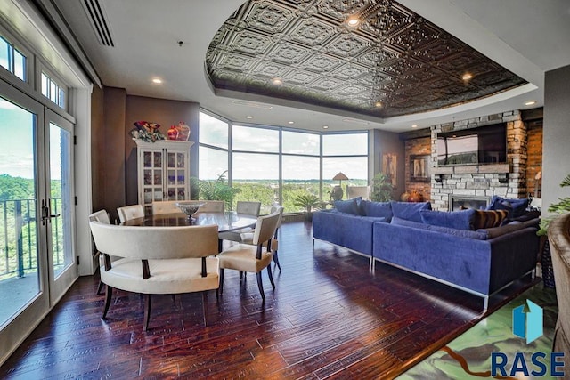 dining space with a healthy amount of sunlight, a tray ceiling, a stone fireplace, and dark wood-type flooring