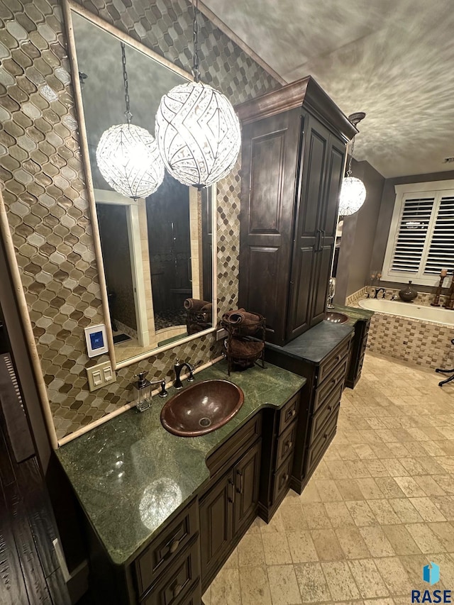 bathroom with vanity, a chandelier, and a relaxing tiled tub