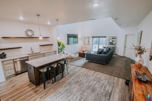 kitchen featuring stainless steel dishwasher, a breakfast bar, sink, decorative light fixtures, and light hardwood / wood-style flooring