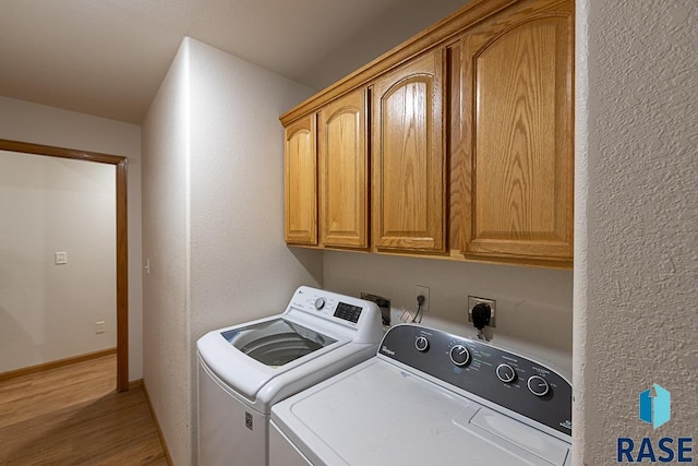 washroom featuring washing machine and clothes dryer, cabinets, and light wood-type flooring