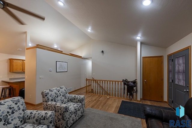 living room with ceiling fan, light hardwood / wood-style floors, and vaulted ceiling