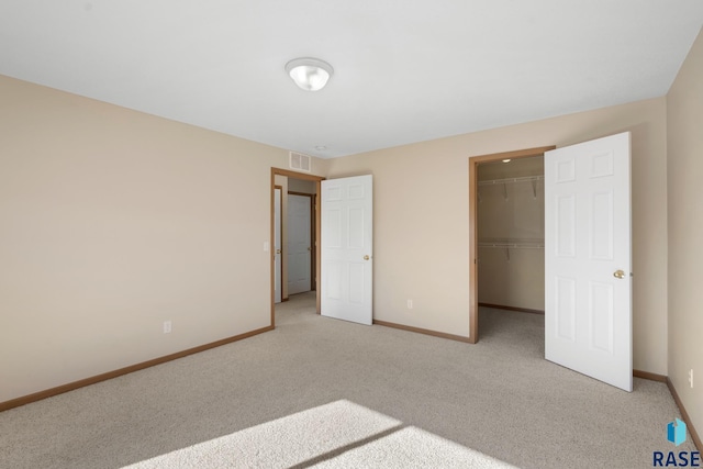 unfurnished bedroom with a walk in closet, a closet, and light colored carpet