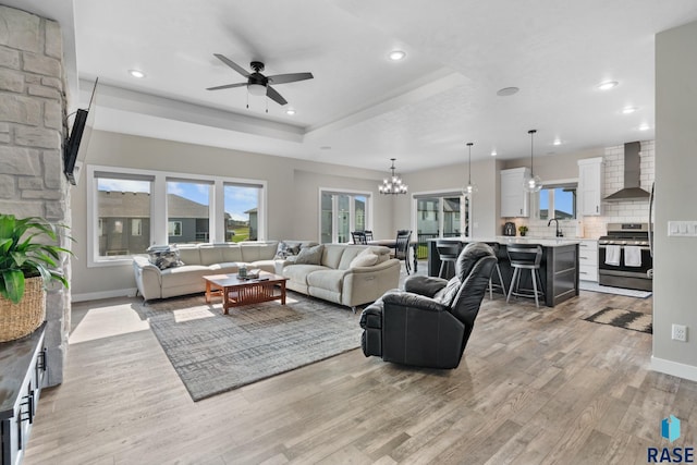 living room with a raised ceiling, light hardwood / wood-style flooring, ceiling fan with notable chandelier, and sink