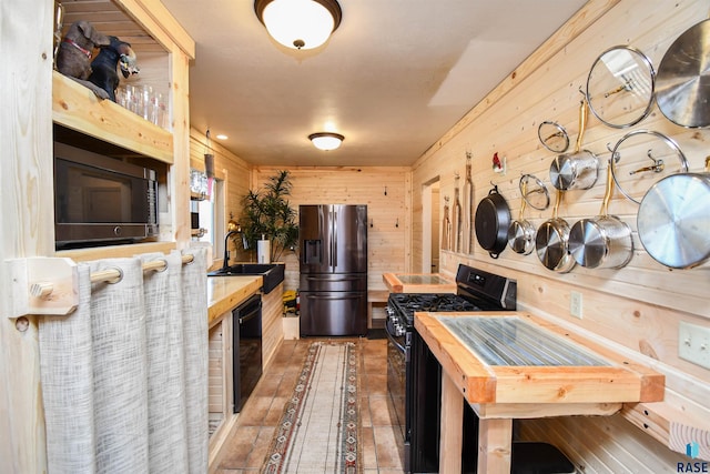 kitchen with black appliances, wood walls, butcher block counters, and sink