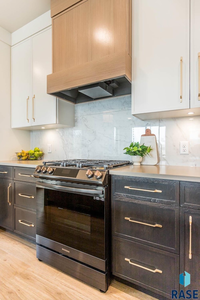 kitchen with premium range hood, tasteful backsplash, gas range, light hardwood / wood-style flooring, and white cabinetry