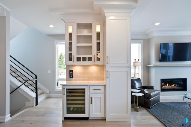 bar with a wealth of natural light, light hardwood / wood-style floors, white cabinetry, and beverage cooler