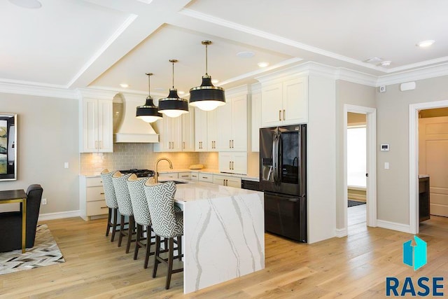 kitchen featuring light wood-type flooring, black refrigerator with ice dispenser, sink, white cabinetry, and an island with sink