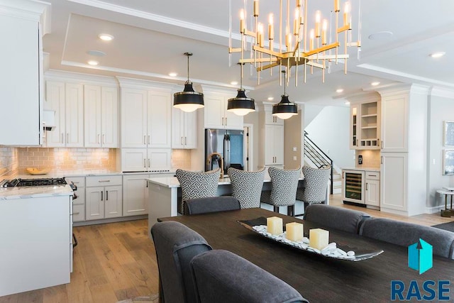 interior space with a raised ceiling, crown molding, beverage cooler, and light wood-type flooring