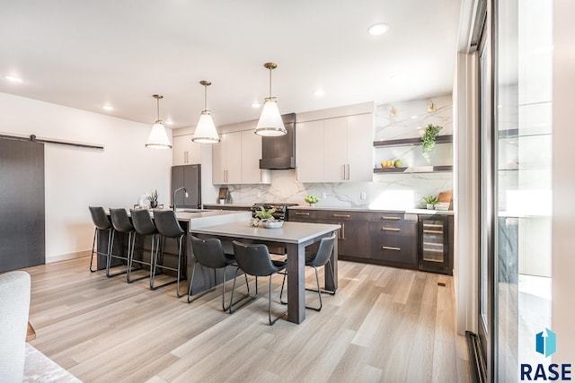 kitchen with a barn door, wine cooler, dark brown cabinets, white cabinets, and light wood-type flooring