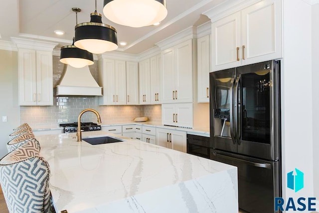 kitchen featuring white cabinetry, sink, hanging light fixtures, light stone counters, and stainless steel fridge