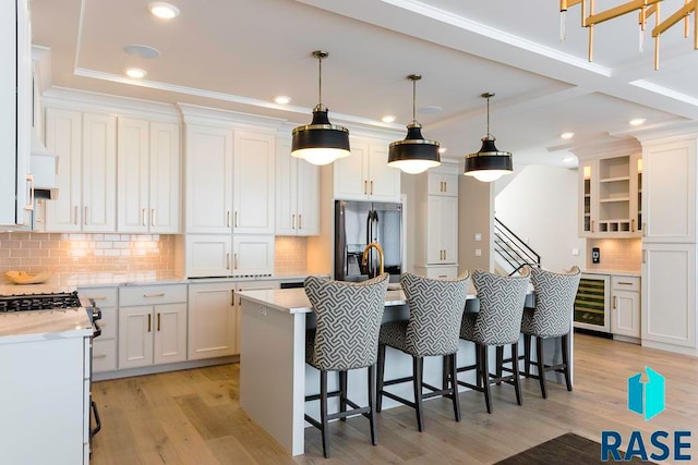 kitchen with a kitchen breakfast bar, light wood-type flooring, white cabinets, stainless steel fridge with ice dispenser, and hanging light fixtures