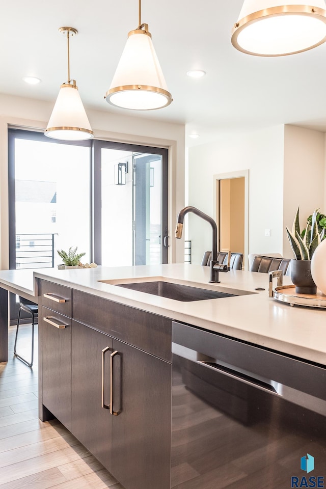 kitchen featuring stainless steel dishwasher, dark brown cabinetry, sink, pendant lighting, and light hardwood / wood-style flooring