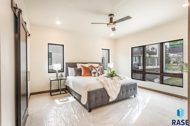 bedroom featuring a barn door, ceiling fan, and light carpet