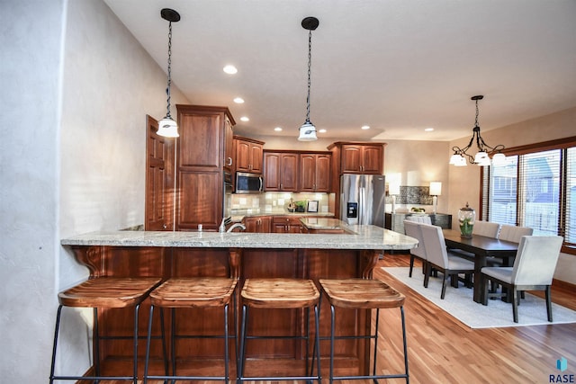 kitchen featuring backsplash, light hardwood / wood-style flooring, appliances with stainless steel finishes, a notable chandelier, and kitchen peninsula