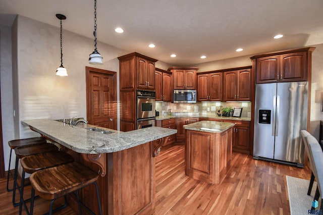 kitchen featuring kitchen peninsula, appliances with stainless steel finishes, pendant lighting, hardwood / wood-style flooring, and a breakfast bar area