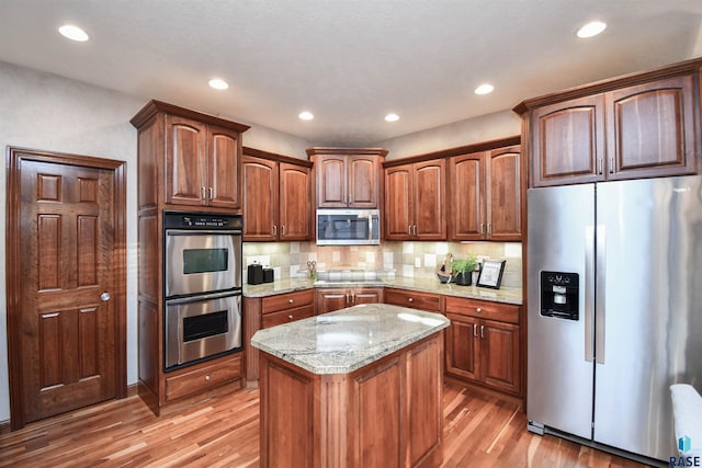 kitchen featuring light stone countertops, appliances with stainless steel finishes, a center island, and light hardwood / wood-style floors