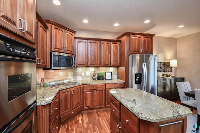 kitchen featuring light stone countertops, a center island, stainless steel appliances, tasteful backsplash, and light hardwood / wood-style floors