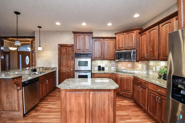 kitchen with pendant lighting, light wood-type flooring, kitchen peninsula, and appliances with stainless steel finishes