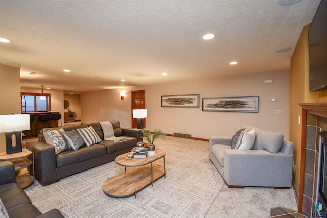 living room featuring a tiled fireplace, light colored carpet, and a textured ceiling