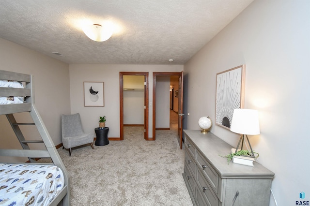 bedroom with a walk in closet, a closet, light colored carpet, and a textured ceiling