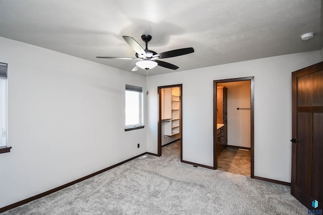 unfurnished bedroom featuring connected bathroom, a spacious closet, ceiling fan, light carpet, and a closet