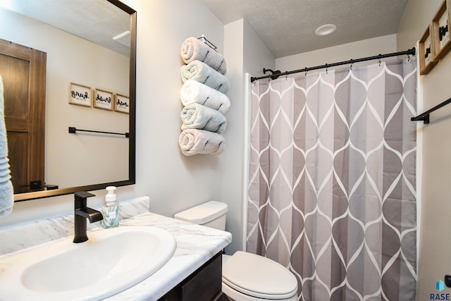 bathroom with a textured ceiling, vanity, toilet, and walk in shower